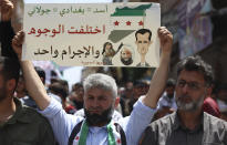 FILE - A Syrian protester holds up a placard during a protest against al-Qaida-linked Hayat Tahrir al-Sham group in Binnish town, in Idlib province, Syria, on May 17, 2024. Syria's devastating civil war, now in its 14th year, remains largely frozen and so are efforts to find a viable political solution to end it, while millions of Syrians have been pulled into poverty, and struggle with accessing food and health care as the economy deteriorates across the country's front lines. Aid organizations are making their annual pitches to donors ahead of a fundraising conference in Brussels for Syria on Monday, May 27. The placard shows drawings of Syrian President Bashar Assad, the late Islamic State group leader Abu Bakr al-Baghdadi and Abu Mohammed al-Golani, leader of the Hayat Tahrir al-Sham, once linked to al-Qaida. The Arabic writing reads: "Assad = Baghdadi = al-Golani. The faces are different but the crime is one." (AP Photo/Ghaith Alsayed, File)