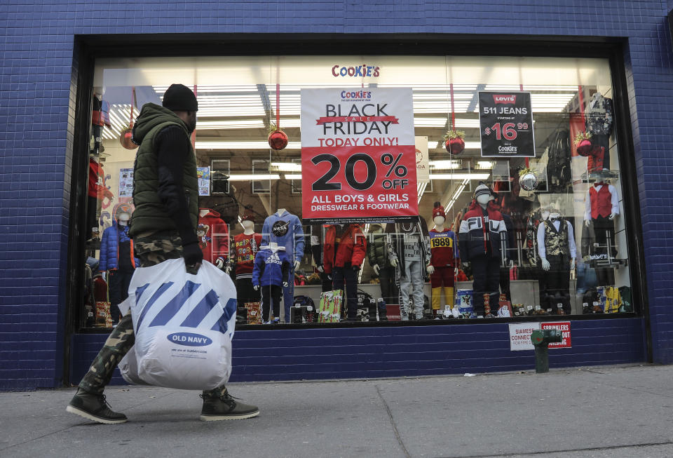 FILE - In this Nov. 29, 2019, file photo people walk by a Black Friday promotional at Cookie's department store in the Brooklyn Borough of New York. Shopping at sales and using coupons may not be saving you as much money as you think. Knowing the pitfalls and having a plan can help keep your holiday shopping from coming back to bite you in January. (AP Photo/Bebeto Matthews, File)