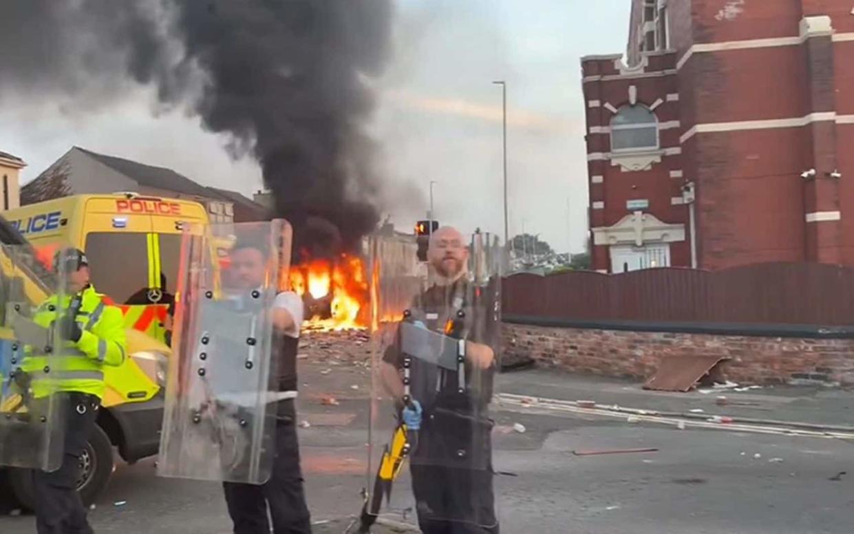 Police hold riot shields as a van burns behind them