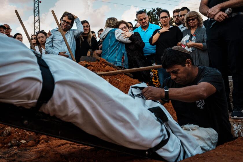 YEHUD, ISRAEL -- OCTOBER 15, 2023: Mirela Ludmir, center, is consoled as the family members mourn and watch the burial of Daniel Levy who was killed in the BeOeri Kibbutz in an unprecedented Hamas assault on communities near Gaza, during DanielOs funeral service at Yehud Cemetery in Yehud, Israel, Sunday, Oct. 15, 2023. OI donOt say this out loud, but I need to ask God why N why was this good man murdered?O said Michael Levy, whose brother Daniel, a 34-year-old Peruvian-born physician and father of two, was killed in his kibbutz just outside Gaza as he tried to tend to the injured around him. Across Israel and inside the Gaza Strip, the sheer scale of death in this conflict is overwhelming the living. Institutions from hospitals to mortuaries. forensics labs to cemeteries are staggering under the weight. At least 1,400 people have been killed in Israel and some 2,800 in Gaza since Oct. 7, when the current war began with a cross-border attack by the militant group Hamas. (MARCUS YAM / LOS ANGELES TIMES)