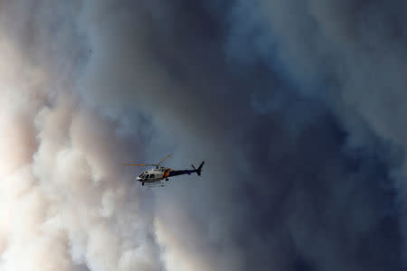 A helicopter flies past smoke from wildfires near Fort McMurray, Alberta, Canada, May 6, 2016. REUTERS/Chris Wattie