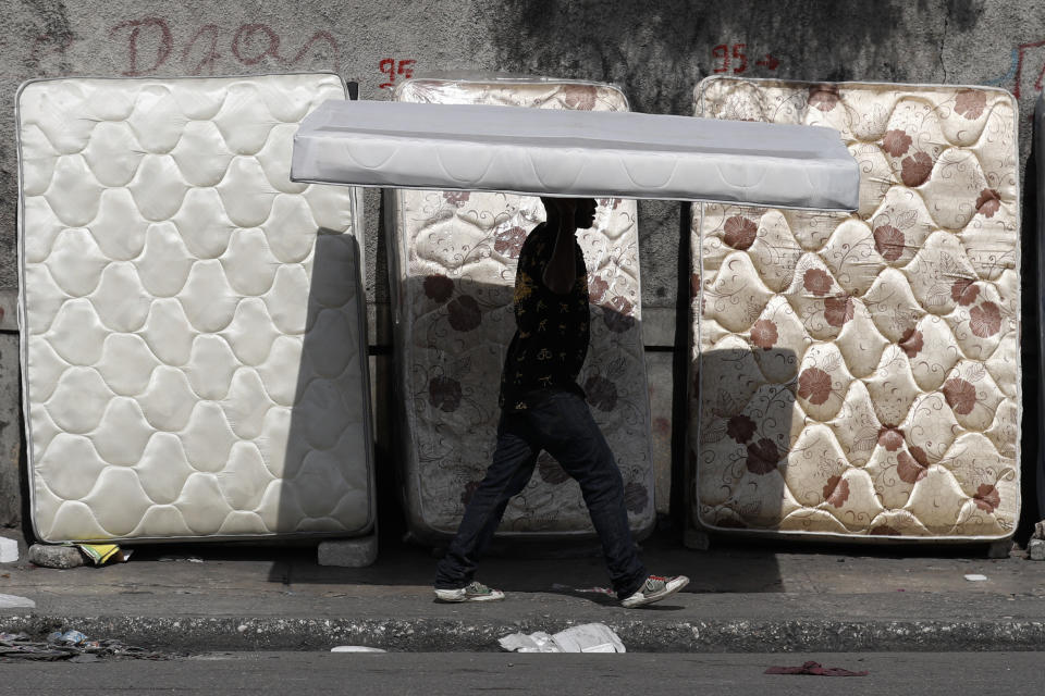 A man balances a mattress on his head past others leaned up for sale alongside a road in Port-au-Prince, Haiti, Wednesday, Oct. 2, 2019. There was a relative pause Wednesday in disturbances that have wracked Haiti's capital for weeks as protesters have tried to drive President Jovenel Moise from power. (AP Photo/Rebecca Blackwell)