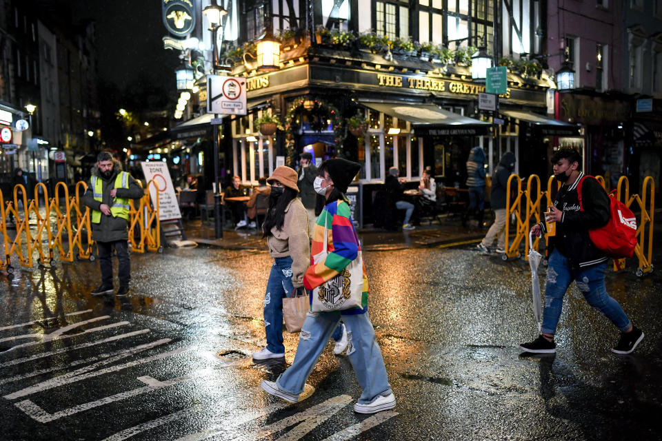 People wearing face masks to protect against coronavirus as they walk past a pub in Soho, London, Monday, Dec. 14, 2020. London and its surrounding areas will be placed under Britain's highest level of coronavirus restrictions beginning Wednesday as infections rise rapidly in the capital, the health secretary said Monday, adding that a new variant of the virus may be to blame for the spread.  (AP Photo/Alberto Pezzali)