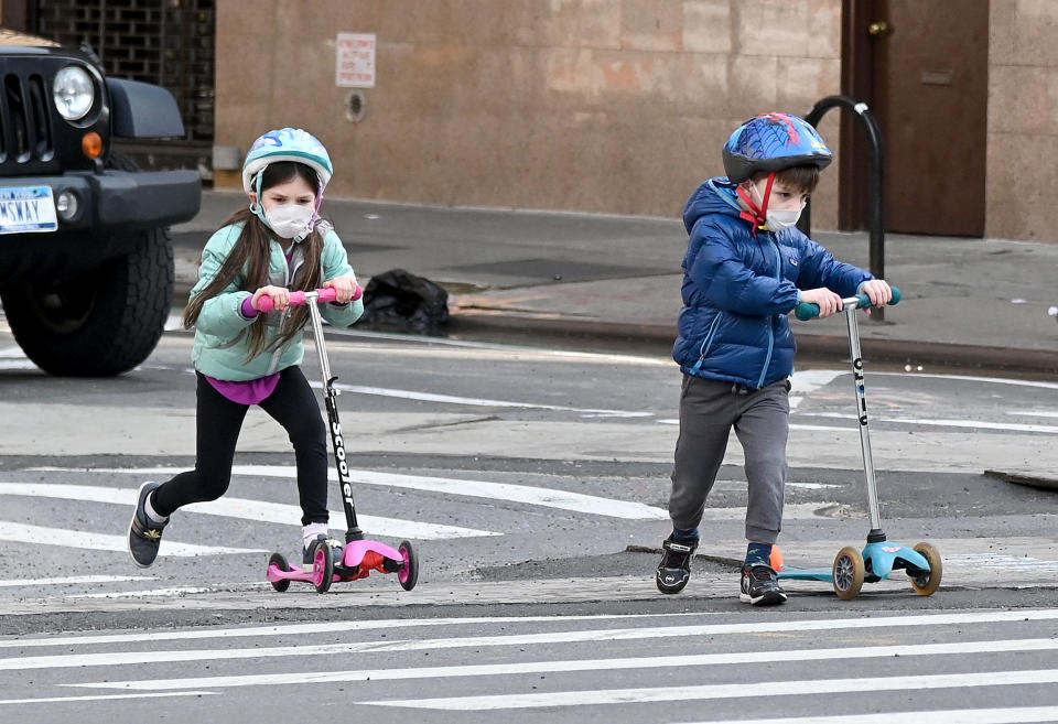 Children wearing face masks play on their scooters during the coronavirus pandemic on April 25, 2020 in New York City. (Photo by Jamie McCarthy/Getty Images)