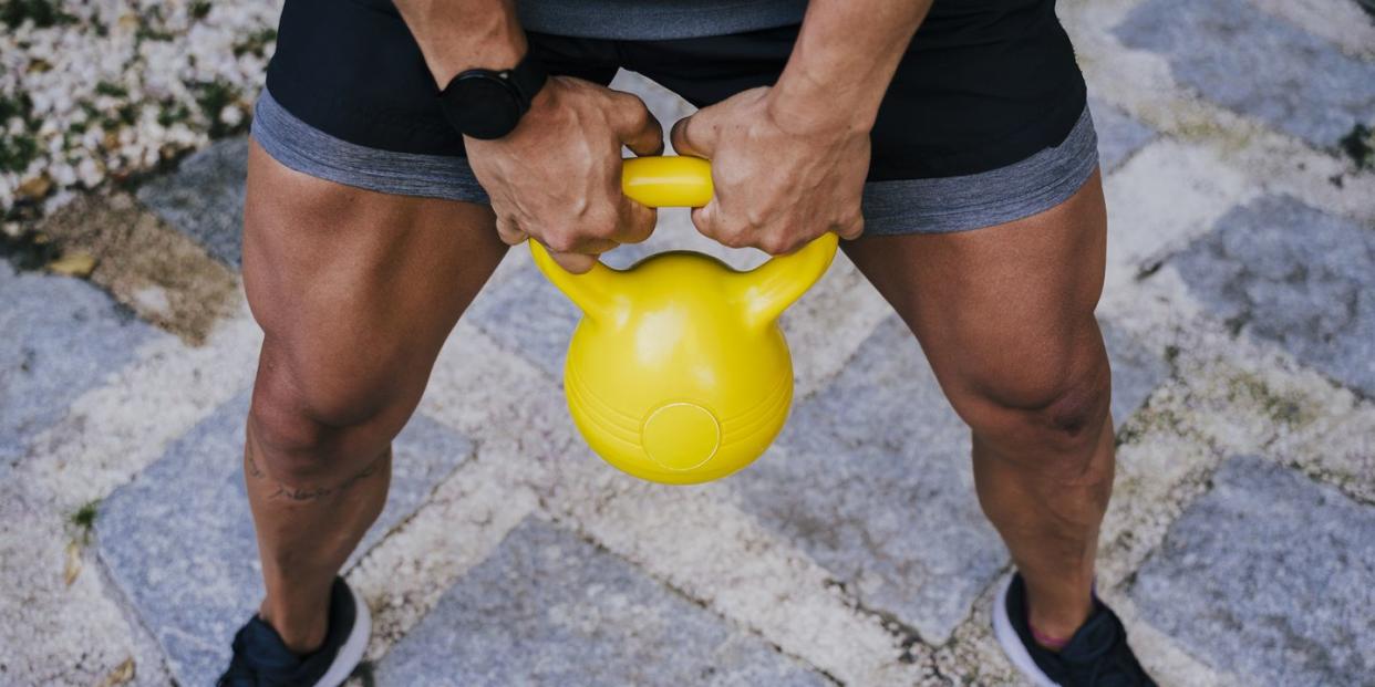 mid adult man lifting kettlebell while standing in yard