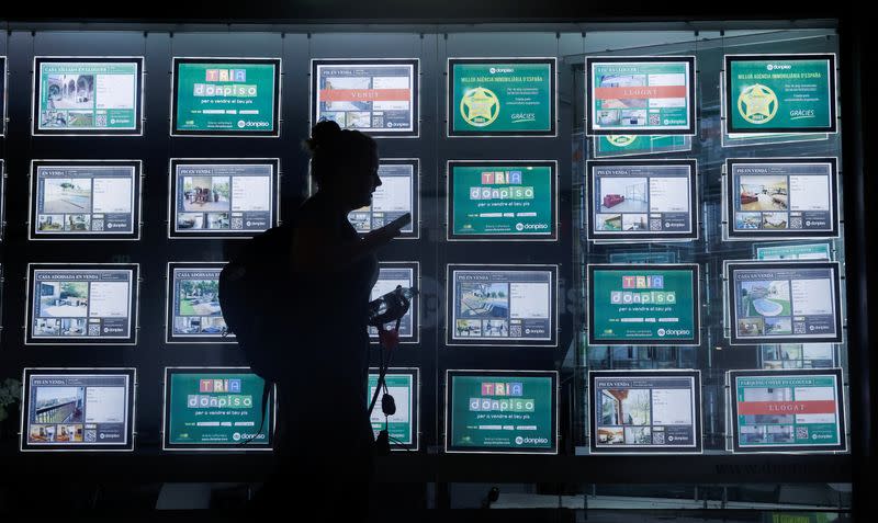 A woman looks her mobile as she walks past a real estate office in El Masnou