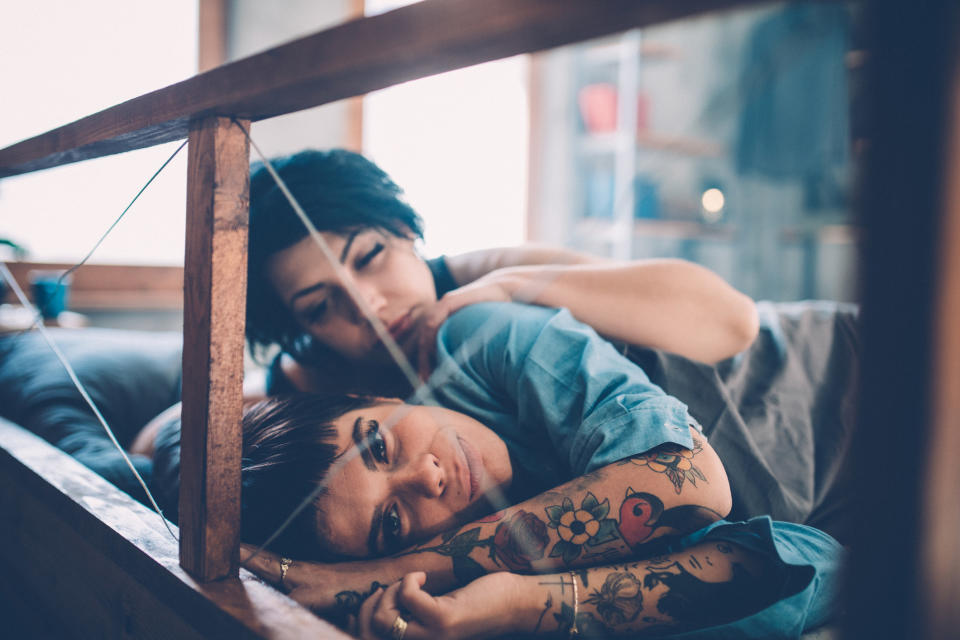 a woman lying in bed and facing the opposite direction of her partner, who has her arm on her shoulder