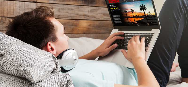 Man watching a streaming series on a laptop while laying in bed.