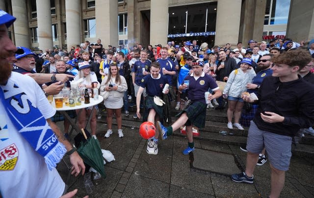 Schottische Fans spielen mit einem Fußball, während andere in der Stuttgarter Innenstadt trinken