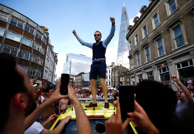 A man in a Gareth Southgate-style waistcoat clambers on the ambulance