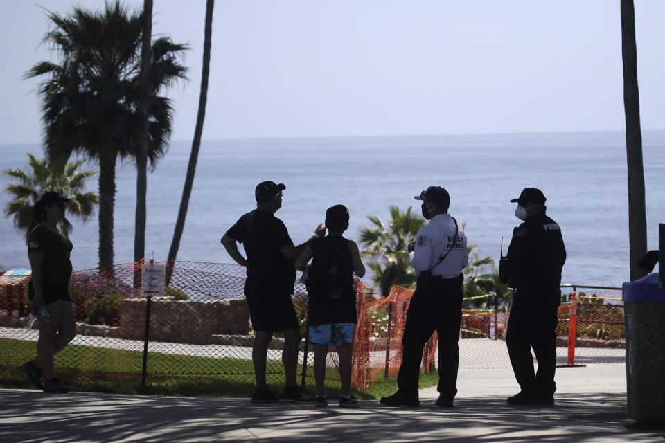 FILE - Visitors talk to police officers in front of a closed-off beach Sunday, May 3, 2020, in Laguna Beach, Calif. Environmental advocates are celebrating in Laguna Beach _ but it won't be with balloons. The hilly, seaside city is weighing a plan to ban the sale and public use of balloons to curtail the risk of devastating wildfires and eliminate a major source of trash floating near the community's scenic shores. (AP Photo/Marcio Jose Sanchez, File)