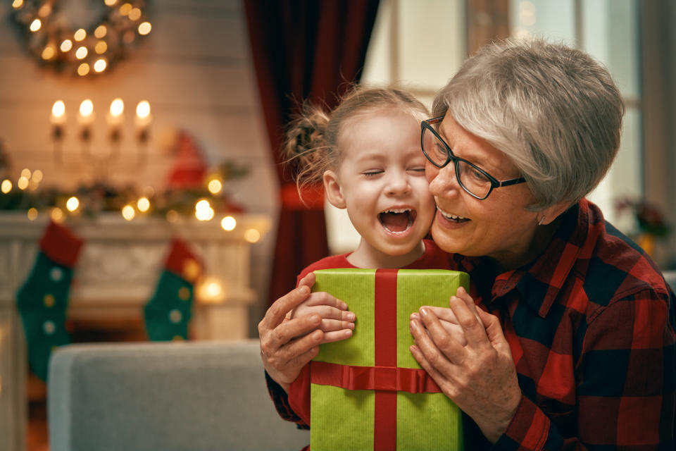 Merry Christmas and Happy Holidays! Cheerful grandma and her cute grand daughter girl exchanging gifts. Granny and little child having fun near tree indoors. Loving family with presents in room.