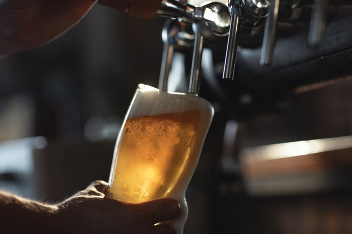 Close-up of a hand holding a beer glass being filled from a tap at a bar