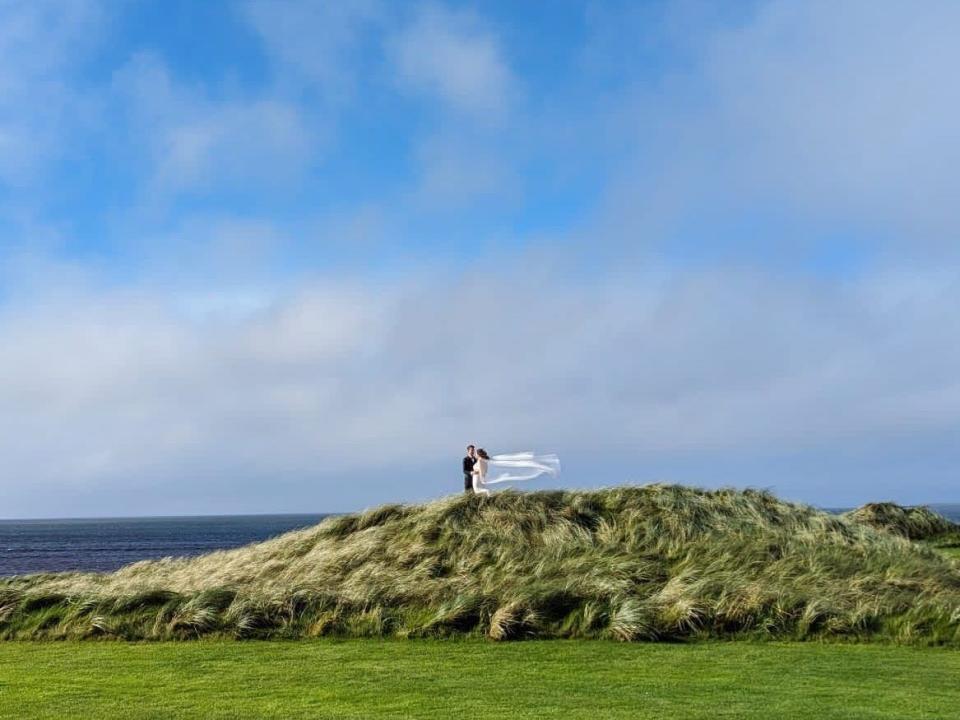 A bride and a groom on top of grassy hill in Ireland with blue skies and sea