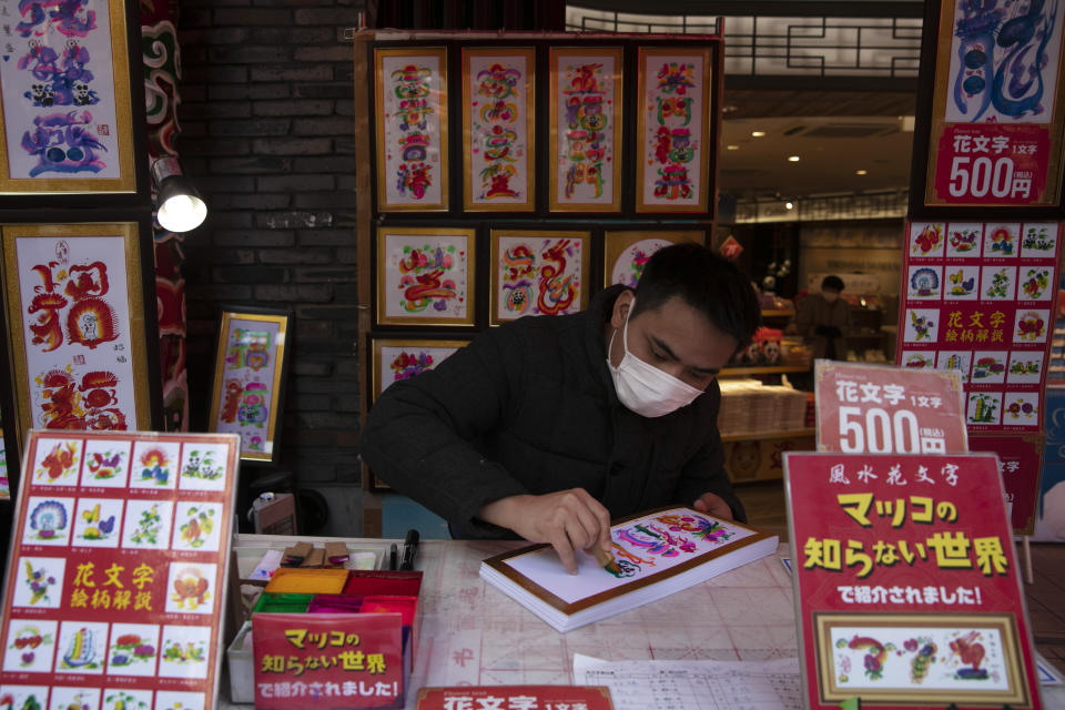 In this Feb. 13, 2020, photo, a vendor wears a mask while writing calligraphy for customers in Yokohama's Chinatown, near Tokyo. A top Olympic official made clear Friday the 2020 Games in Tokyo will not be cancelled despite the virus that has spread from China. (AP Photo/Jae C. Hong)