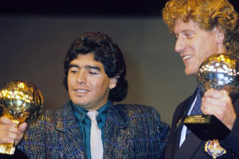 Maradona mira con orgullo el Balón de Oro que recibió en 1986 como mejor futbolista del Mundial de México. Junto a él sonríe el arquero alemán Toni Schumacher, ganador del Balón de Plata