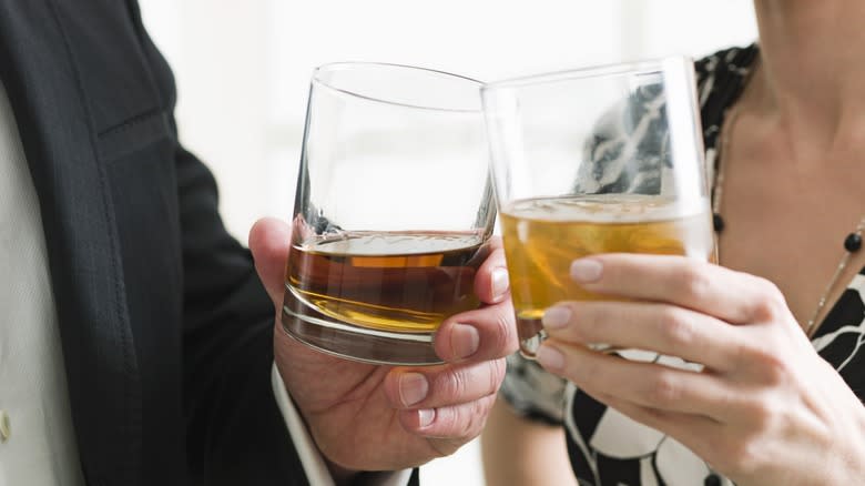 Two people cheersing two glasses of whiskey