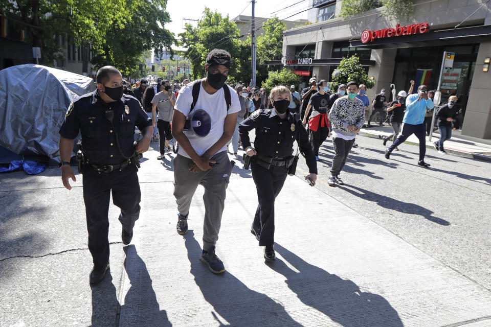 A protester who did not give his name walks with Seattle Police assistant chiefs Adrian Diaz, left, and Deanna Nollette, right, Thursday, June 11, 2020, inside what is being called the "Capitol Hill Autonomous Zone" in Seattle. The officers were attempting to walk to the department's East Precinct building, which has been boarded up and abandoned except for a few officers inside, but the protester, in a move that angered some other protesters, said he would walk with the officers to a side entrance of the precinct rather than have them walk directly through a crowd of angry protesters.(AP Photo/Ted S. Warren)