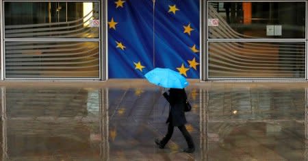 A woman holds an umbrella as she walks past the flag of the European Union outside the European Commission in Brussels, Belgium, December 13, 2017. REUTERS/Phil Noble