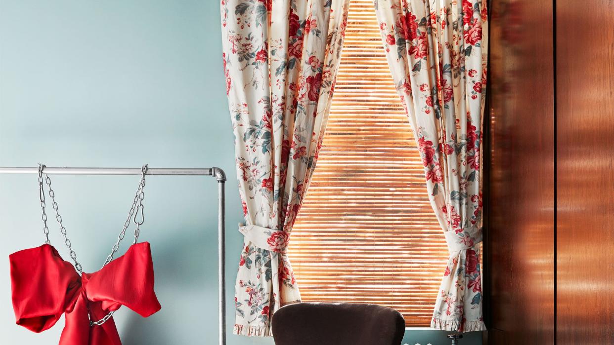 short curtains in a blue room with a red dress in chains on rack next to it