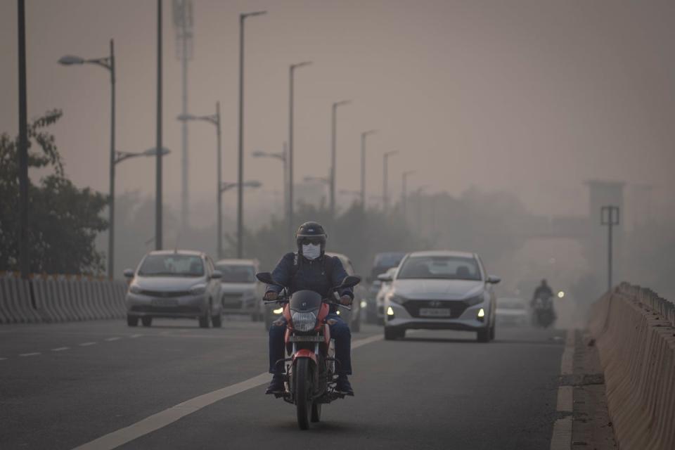 A motorcyclist wearing a pollution mask drives through smog in Delhi (AP)