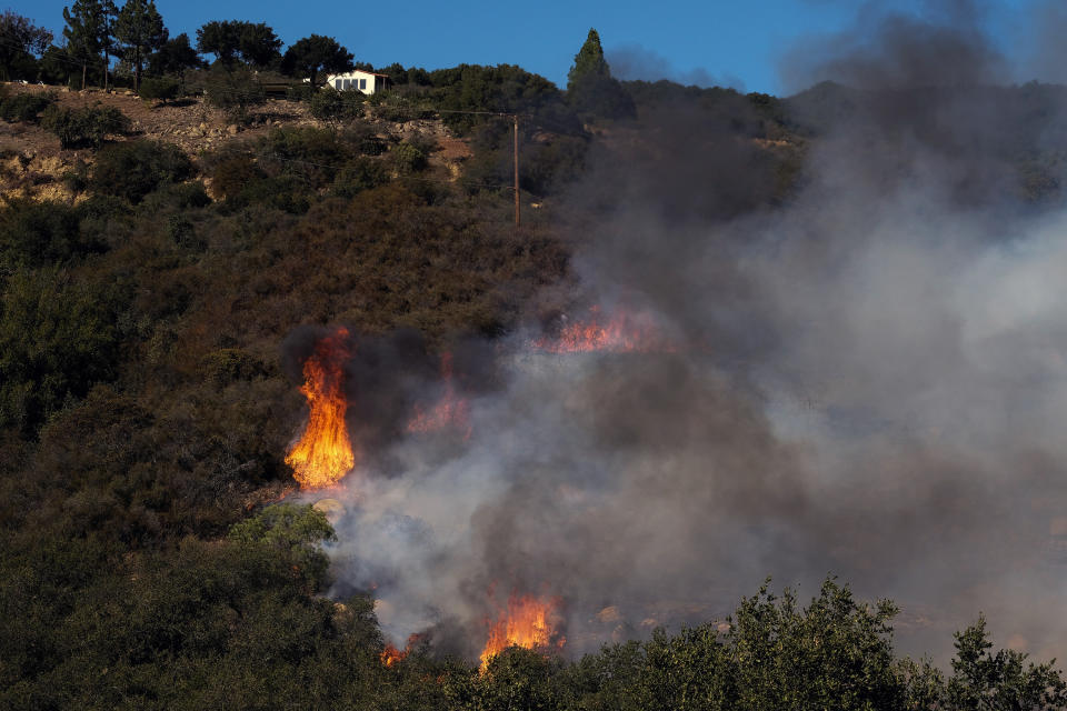 A wildfire burns near a home Wednesday, Oct. 13, 2021, in Goleta, Calif. A wildfire raging through Southern California coastal mountains threatened ranches and rural homes and kept a major highway shut down Wednesday as the fire-scarred state faced a new round of dry winds that raise risk of flames. The Alisal Fire covered more than 22 square miles (57 square kilometers) in the Santa Ynez Mountains west of Santa Barbara. (AP Photo/Ringo H.W. Chiu)