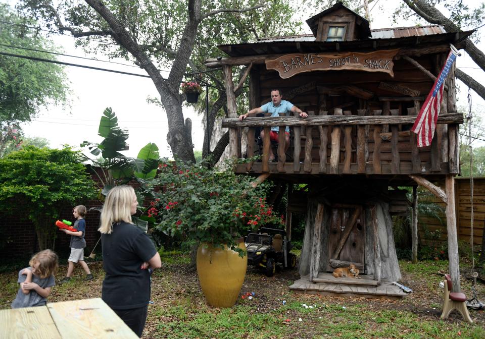 Jason Barnes, top right, sits in his kids' treehouse while his family plays in their backyard April 18, 2020.