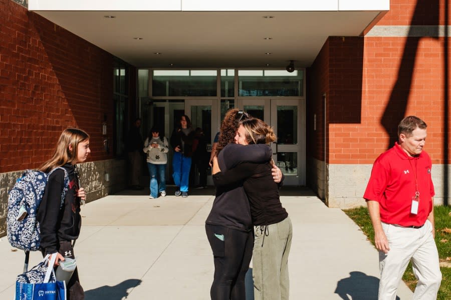 A parent and teacher embrace outside at Tuscarawas Valley Middle/High School, Tuesday, Nov. 14, 2023, in Zoarville, Ohio, as children are gradually let out of school early. A charter bus filled with high school students was rear-ended by a semitruck on an Ohio highway earlier in the day, leaving several people dead and multiple others injured. (Andrew Dolph/Times Reporter via AP)