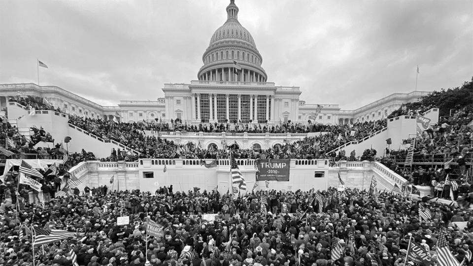 Black-and-white image of U.S. Capitol surrounded by thousands of people holding Trump flags and banners and American flags.