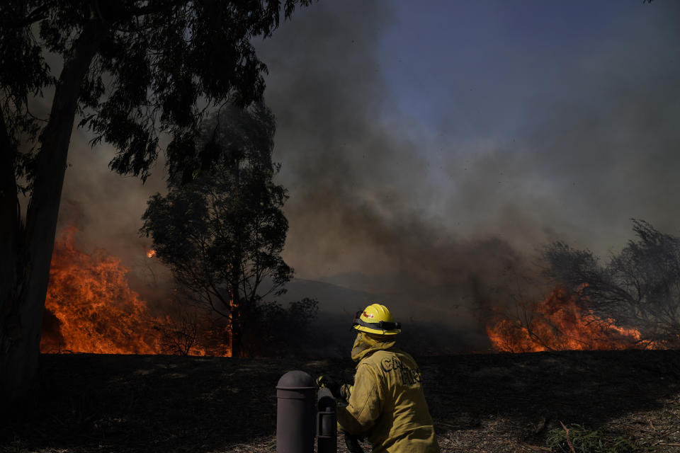 A firefighter watches flames from the Silverado Fire, Monday, Oct. 26, 2020, in Irvine, Calif. A fast-moving wildfire forced evacuation orders for 60,000 people in Southern California on Monday as powerful winds across the state prompted power to be cut to hundreds of thousands to prevent utility equipment from sparking new blazes. (AP Photo/Jae C. Hong)