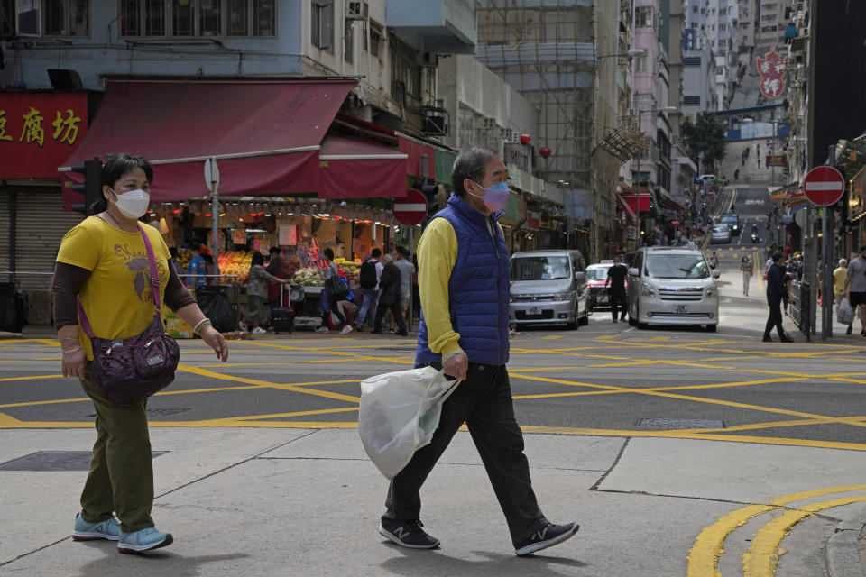 People wearing face masks walk along a street in Hong Kong, Sunday, March 13, 2022. The territory's leader, Chief Executive Carrie Lam, warned the peak of the latest surge in coronavirus infections might not have passed yet. (AP Photo/Kin Cheung)