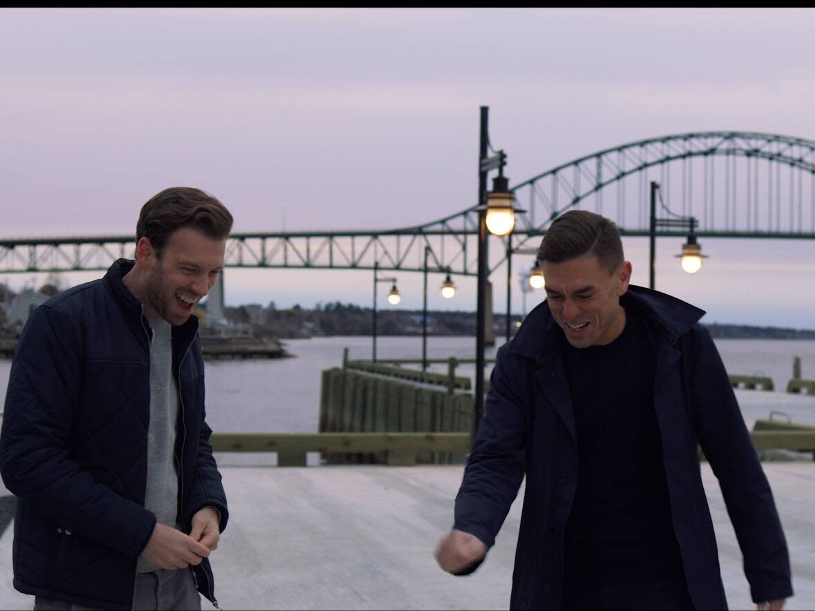 Adam Lordon, left, and James Mullinger, with Miramichi's Centennial Bridge in the background, during filming of Atlantic Edition, which Lordon directs and Mullinger produces. The pair are teaming up on a new sitcom set in Miramichi. (Submitted by Adam Lordon - image credit)