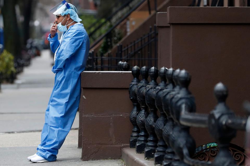 FILE - Emergency room nurse Brian Stephen leans against a stoop as he takes a break from his work at the Brooklyn Hospital Center, Sunday, April 5, 2020, in New York. The worldwide surge in coronavirus cases driven by the new omicron variant is the latest blow to already strained hospitals, nursing homes, police departments and supermarkets struggling to maintain a full contingent of nurses, police officers and other essential workers as the pandemic enters its third year. (AP Photo/Kathy Willens, File)