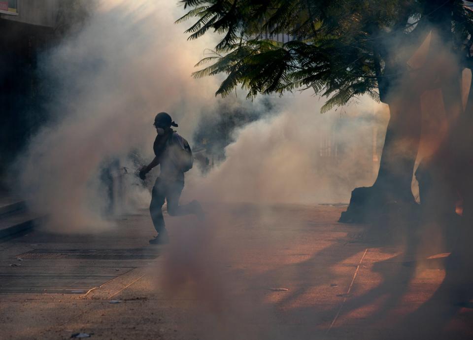 A demonstrator take cover from tear gas fired by Bolivarian National police during clashes with anti-government protesters in Caracas,Venezuela, Saturday, March 8, 2014. The Venezuelan government and opposition appear to have reached a stalemate, in which street protests continue almost daily while the opposition sits out a peace process it calls farcical. (AP Photo/Fernando Llano)