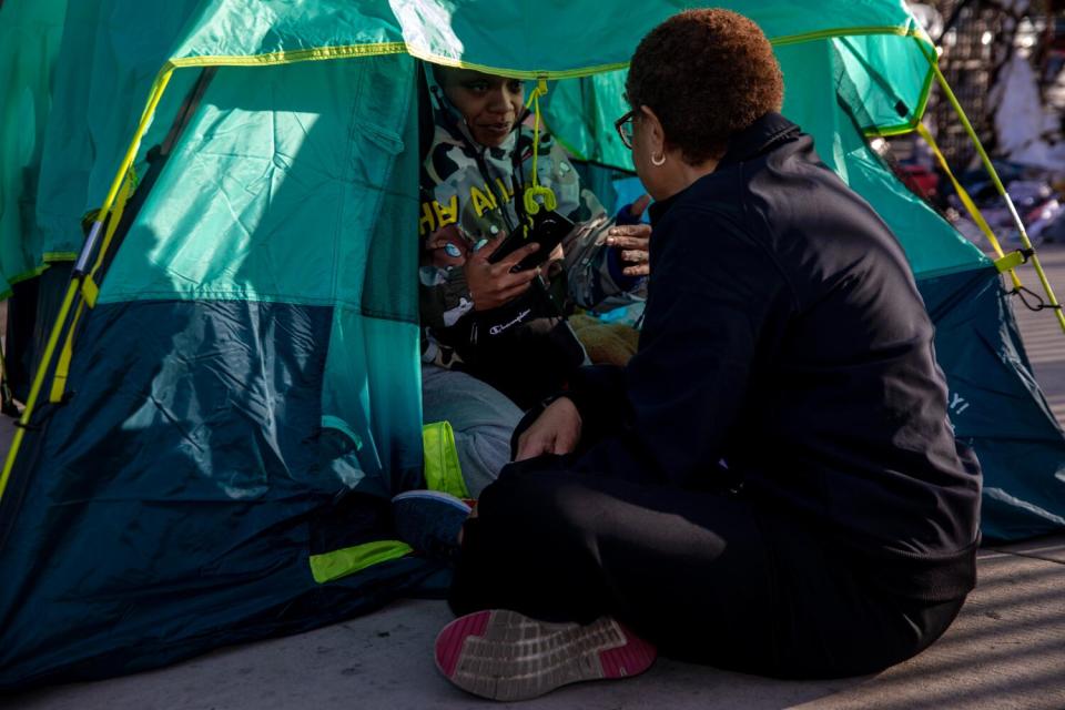 Mayor Karen Bass kneels to talk to a person in a tent.