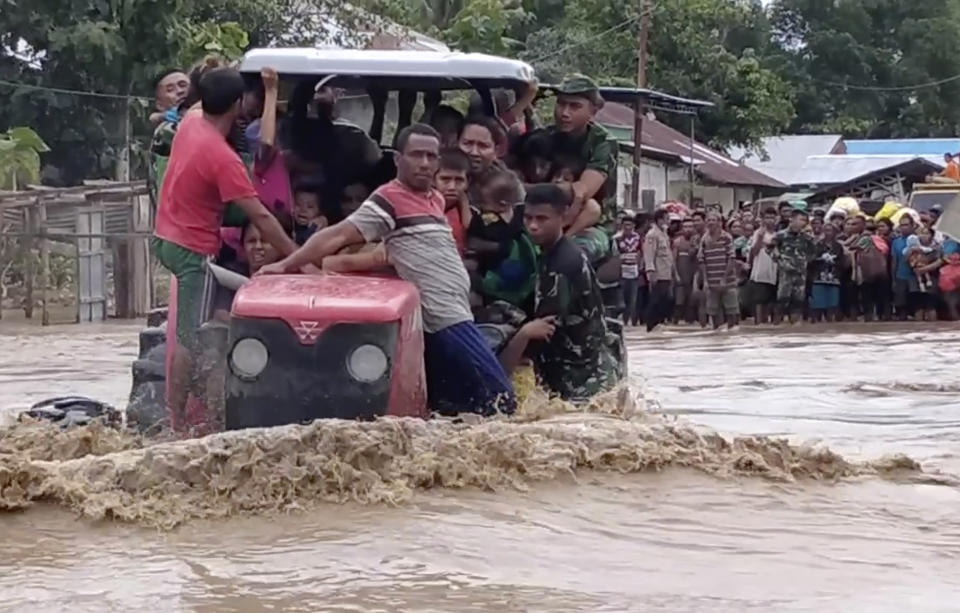In this image made from video, Indonesian soldiers use a tractor to help residents to cross a flooded road in Malaka Tengah, East Nusa Tenggara province, Indonesia, Monday, April 5, 2021. Multiple disasters caused by torrential rains in eastern Indonesia have left dozens of people dead and missing and displaced thousands, the country's disaster relief agency said Monday. (AP Photo)