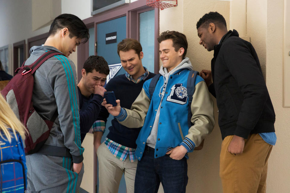 A group of teens looking at a guy's phone