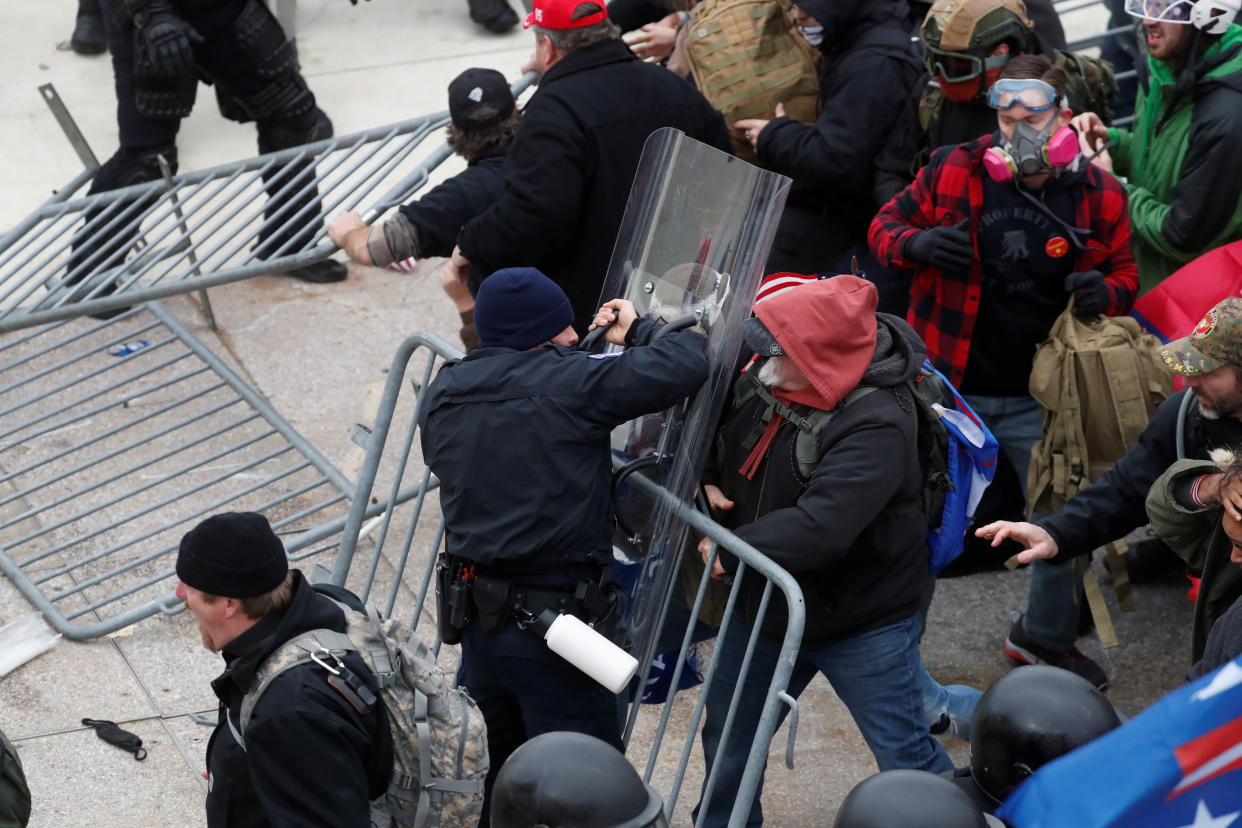 Pro-Trump protesters break down barricades on the Capitol steps, and two people, one holding a plastic shield, tussle on either side of a barricade, as helmeted officers look on.