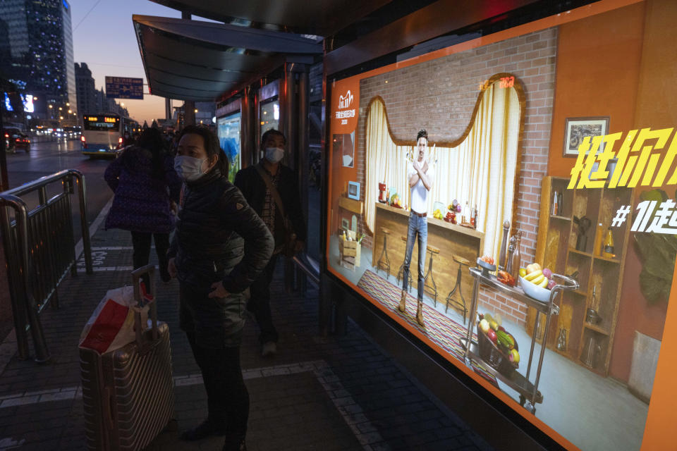 Residents wearing masks to protect from the coronavirus stand near an ad promoting the Nov. 11 Sales Day in Beijing on Sunday, Nov. 8, 2020. Chinese consumers are expected to spend tens of billions on everything from fresh food to luxury goods during this year's Singles' Day online shopping festival, as the country recovers from the coronavirus pandemic.(AP Photo/Ng Han Guan)