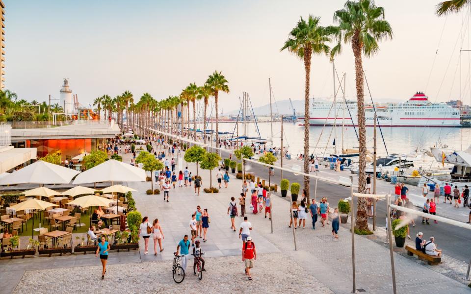 People walk on the restaurant and palm tree that line the seafront promenade Paseo del Mullene Uno in central Malaga