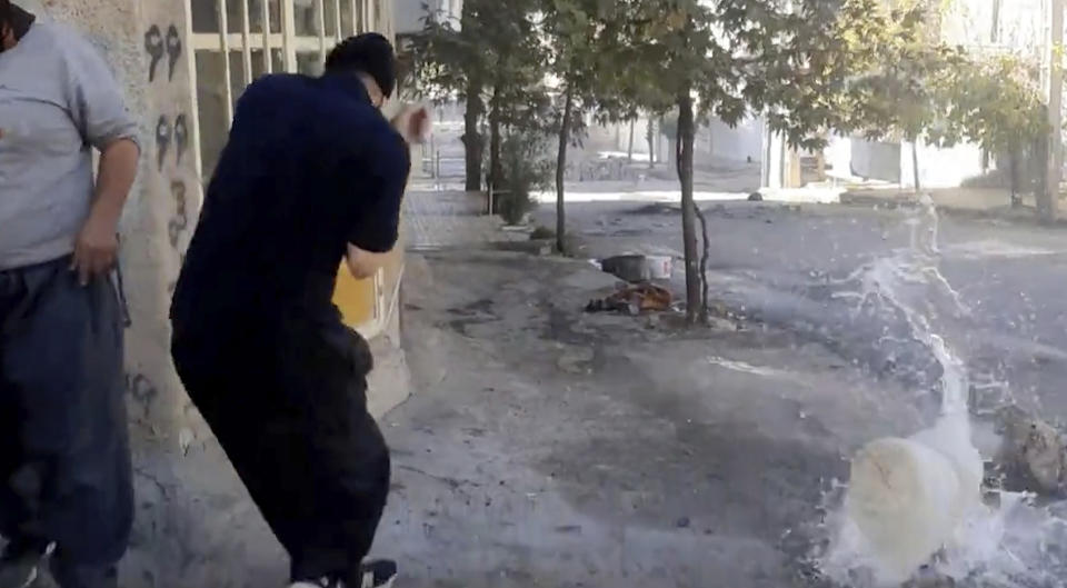 In this image from video provided by Hengaw Organization for Human Rights, a protester reacts after a water container was hit by a bullet during a protest in Javanroud, a Kurdish town in western Iran, Monday, Nov. 21, 2022. (Hengaw Organization for Human Rights via AP)