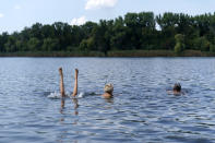 Anastasiia Aleksandrova, 12, left, plays in the water while swimming with her grandparents, Olena, and Andreii, right, at a lake in Sloviansk, Donetsk region, eastern Ukraine, Monday, Aug. 8, 2022. With cities largely emptied after hundreds of thousands have evacuated to safety, the young people that remain face alienation, loneliness and boredom as unlikely yet painful counterpoints to the fear and violence Moscow has unleashed on Ukraine. (AP Photo/David Goldman)