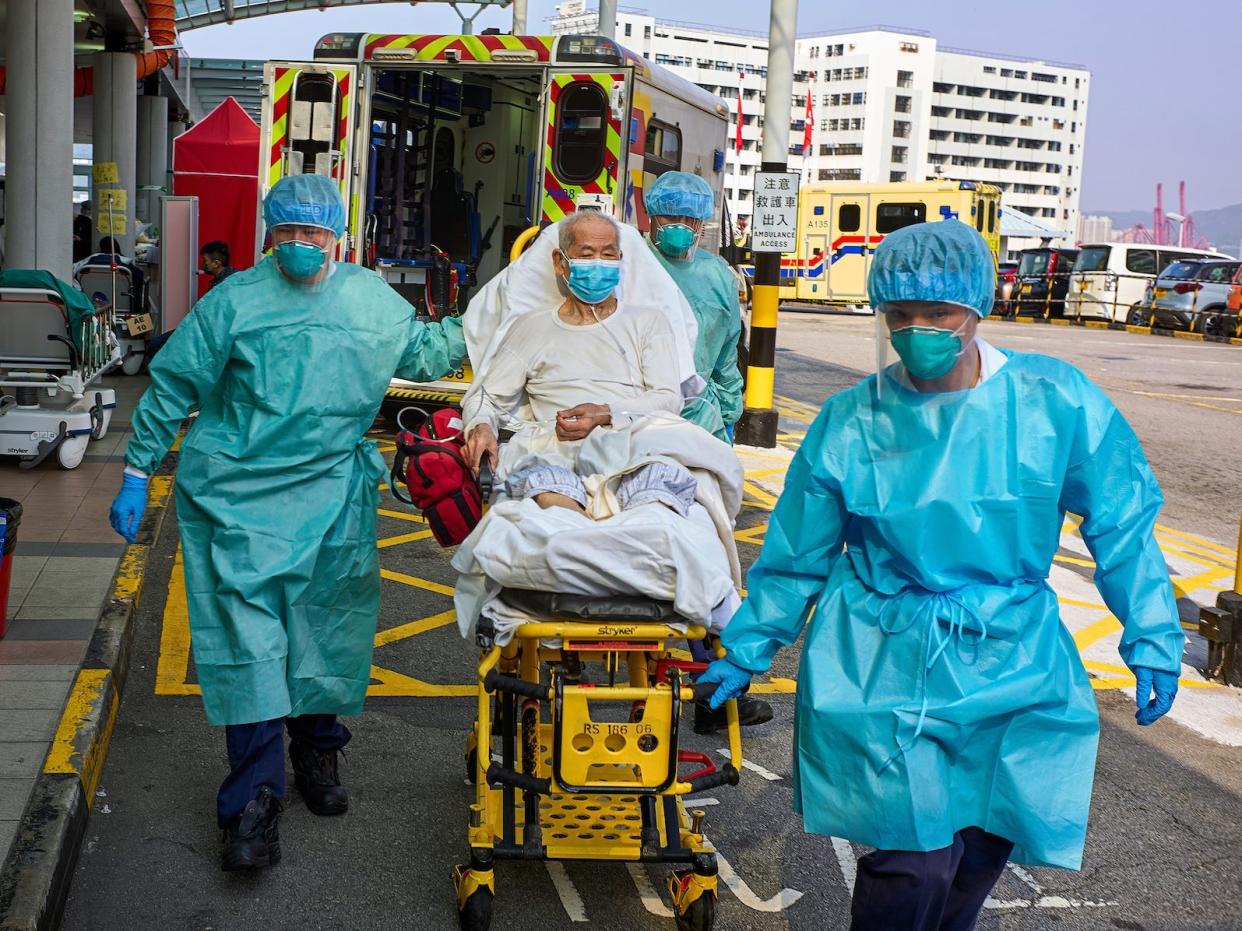 hopsital workers in PPE rushing an elderly patient from ambulance to hospital in hong kong