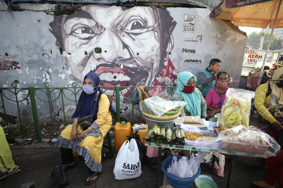 Indonesian women wearing masks as a precaution against the coronavirus outbreak sit at a food stall near a mural in Jakarta, Indonesia, Monday, Sept. 21, 2020. (AP Photo/Dita Alangkara)