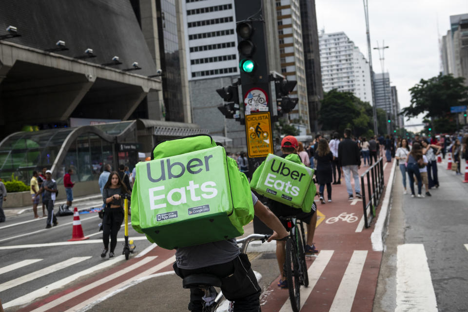 São Paulo, Brazil - April 14, 2019: Two young men working for Uber Eats cycle down Avenida Paulista, a major thoroughfare in São Paulo, delivering food carried in backpacks.