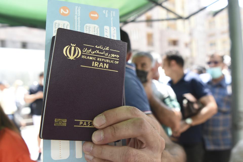 A person holds up an Iranian passport as people, most of them residents of Iran stand in line for a vaccine at a mobile vaccination station in the center of Yerevan , Armenia, Friday, July 9, 2021. Armenia’s offer of free coronavirus vaccines to any foreign visitor has drawn many people from neighboring Iran and other countries to the ex-Soviet Caucasus nation. The Iranians initially visited the Armenian border city of Meghri to get the shots, but the Armenian authorities have decided earlier this week that all foreign nationals should get the shots in the Armenian capital, Yerevan. (Lusi Sargsyan/PHOTOLURE via AP)