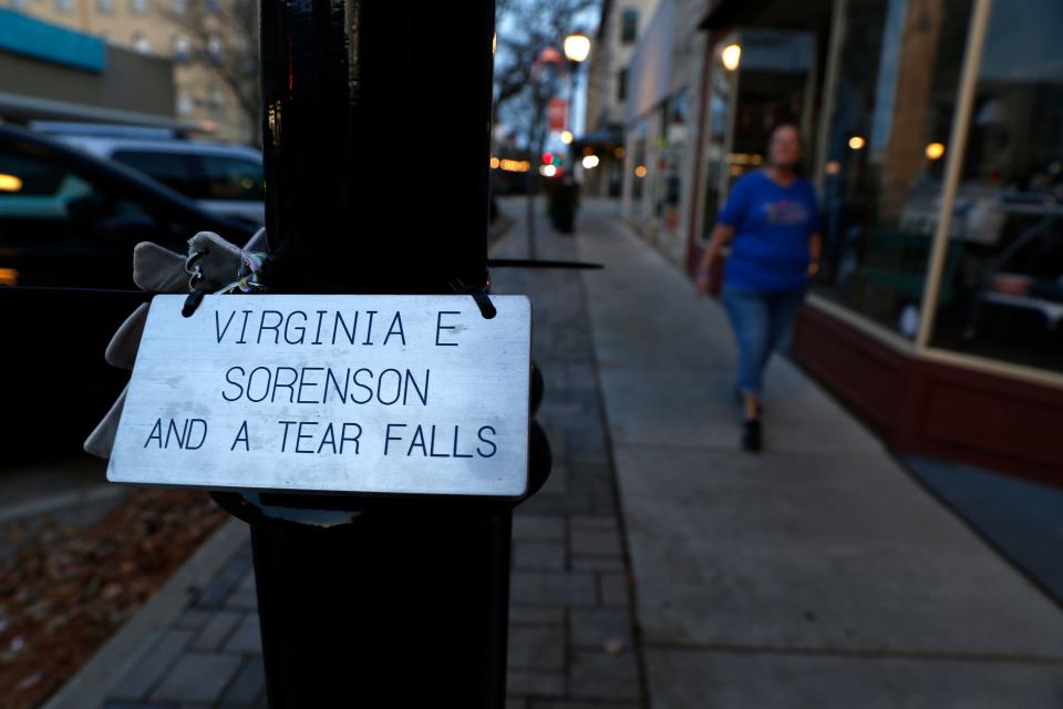 A plaque honoring Virginia “Ginny” Sorenson rests on a lamp post on Thursday, Nov. 3, 2022, along Main Street in Waukesha, Wis., as Donna Kalik walks nearby. Sorenson was a leader and member of the Milwaukee Dancing Grannies who was killed when the driver of an SUV sped through a Christmas parade in Waukesha last November, killing six and injuring dozens of other people. There is a plaque for each of the dead along the parade route. Several new members have joined the Grannies since the incident, including Kalik, who has become the group’s volunteer coordinator. She was at the parade last year and felt compelled to support the Grannies. “It was like a war zone,” she said of the scene the driver left in his wake.