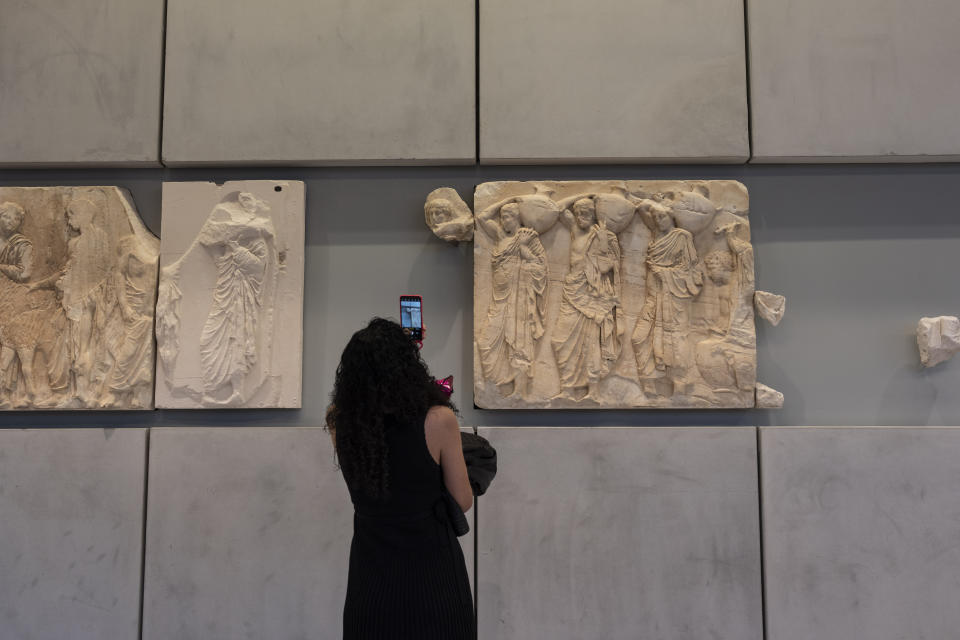 A woman takes a pictures of a newly placed male head on the frieze of the Acropolis museum during a ceremony for the repatriation of three sculpture fragments, in Athens, on Friday, March 24, 2023. Greece received three fragments from the ancient Parthenon temple that had been kept at Vatican museums for two centuries. Culture Ministry officials said the act provided a boost for its campaign for the return of the Parthenon Marbles from the British Museum in London. (AP Photo/Petros Giannakouris)