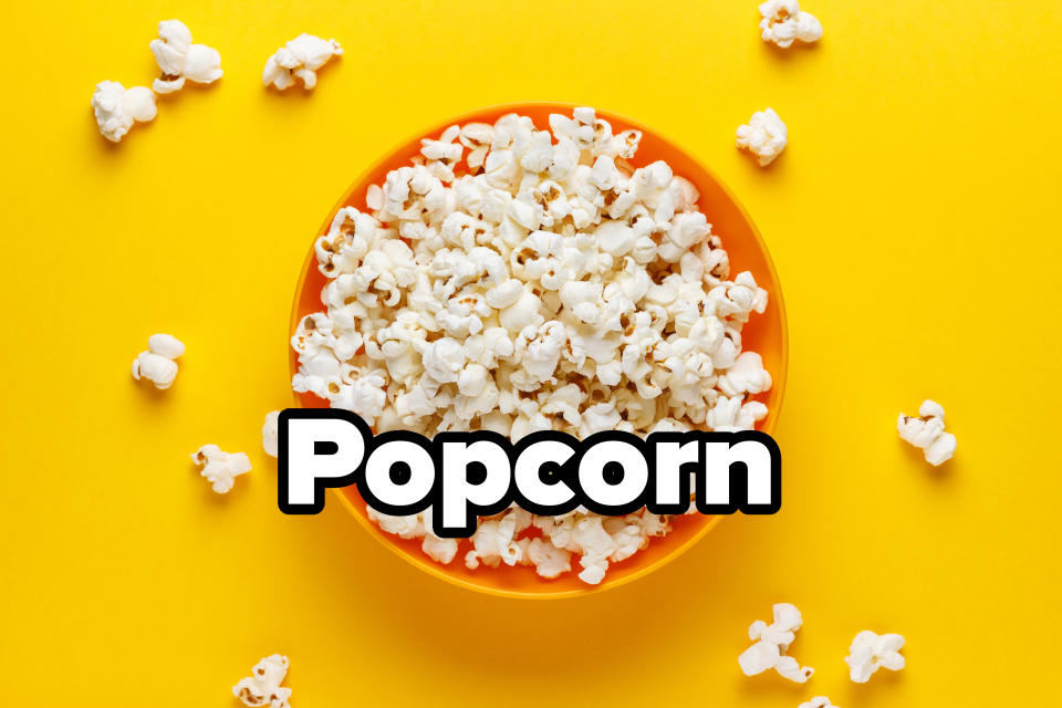 A bowl of popcorn surrounded by scattered popcorn pieces on a solid background