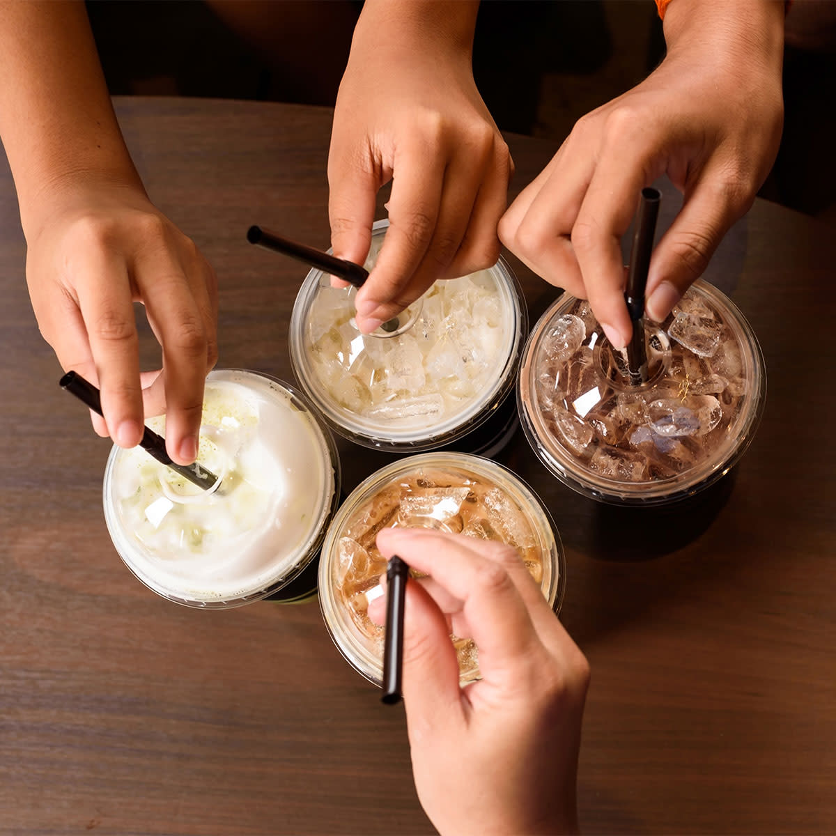 four people stirring iced coffee with straws